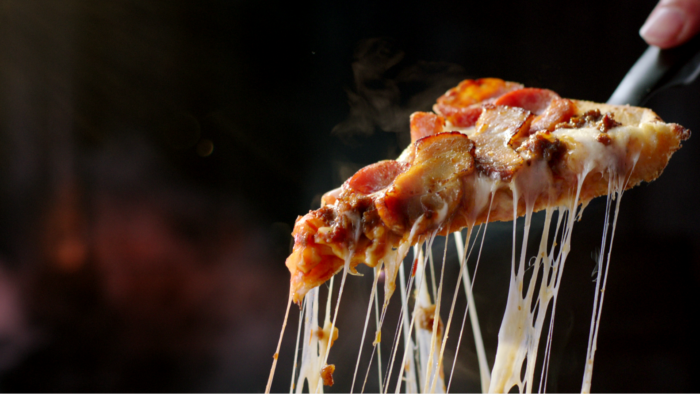 A steaming hot slice of pizza is lifted by a spatula, cheese stretching, in this shot colour graded by Angela Cerasi and directed by Ronald Koetzier