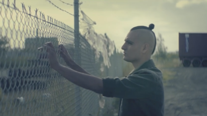 Peachy Keen Colourist Angela Cerasi colour graded this shot of a man with a top-knot holding onto a chainlink fence in a desolate industrial area, for the music video for the song "Lanterns" by the band Birds of Tokyo