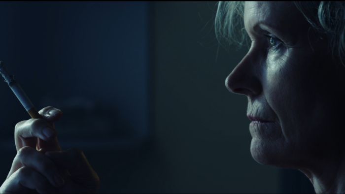 Angela Cerasi's blue-toned colour grade of the character Simone, played by Barbara Bingham, holding a cigarette, for the short film "Over the Edge"